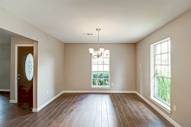 empty room with a notable chandelier, plenty of natural light, and dark wood-type flooring