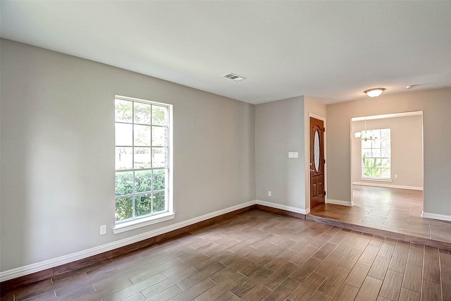 unfurnished room featuring a notable chandelier, dark wood-type flooring, and a wealth of natural light