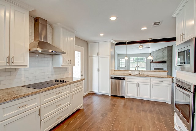 kitchen featuring white cabinets, wall chimney range hood, sink, and appliances with stainless steel finishes