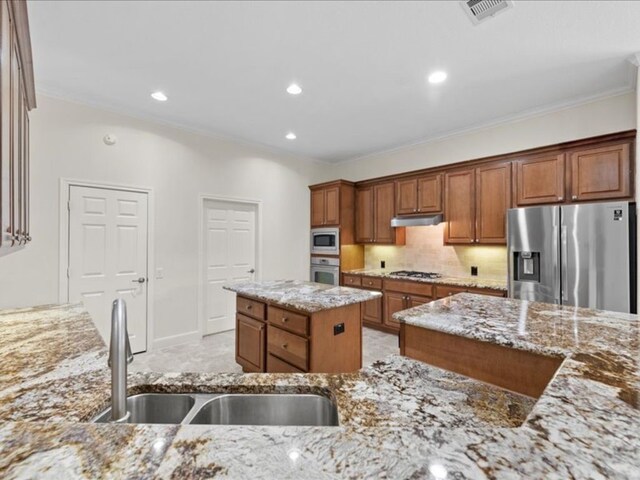 9410 Trinity Trail Ct, Cypress, TX 77433 - kitchen with stainless steel appliances, a sink, under cabinet range hood, light stone counters, and ornamental molding