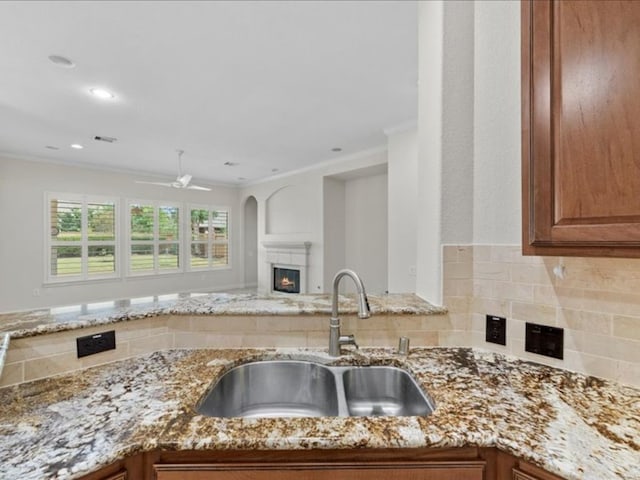 kitchen with ceiling fan, backsplash, light stone countertops, crown molding, and sink