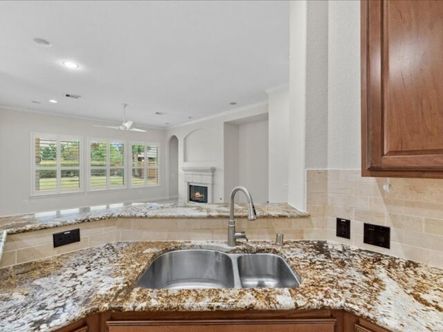9410 Trinity Trail Ct, Cypress, TX 77433 - kitchen featuring a sink, light stone counters, a glass covered fireplace, brown cabinetry, and crown molding
