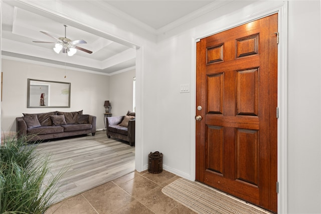 tiled entrance foyer featuring ornamental molding, a tray ceiling, and ceiling fan