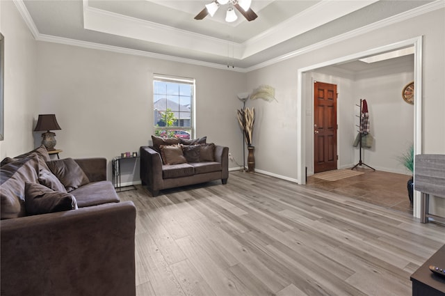 living room featuring ornamental molding, a tray ceiling, light wood-type flooring, and ceiling fan