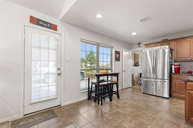 kitchen featuring backsplash, light tile patterned floors, and stainless steel fridge