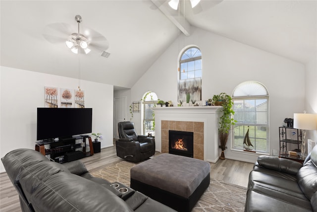 living room with beamed ceiling, light hardwood / wood-style flooring, a tiled fireplace, and ceiling fan