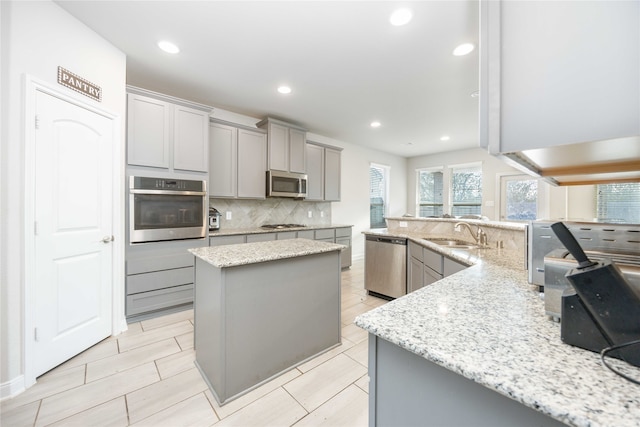 kitchen featuring stainless steel appliances, light stone countertops, gray cabinetry, and a center island