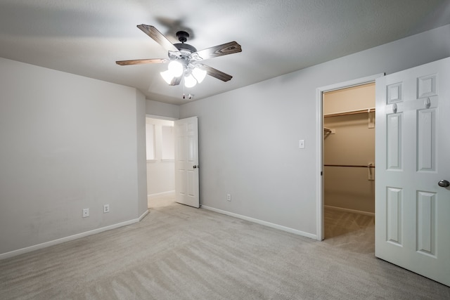 unfurnished bedroom with light carpet, a walk in closet, a closet, and ceiling fan