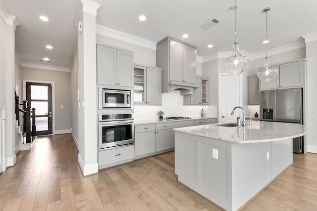 kitchen featuring sink, stainless steel appliances, light hardwood / wood-style flooring, crown molding, and a center island with sink