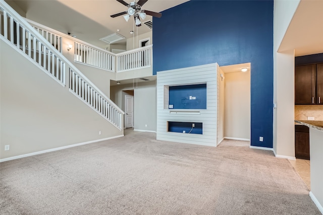 unfurnished living room featuring light carpet, a towering ceiling, a fireplace, and ceiling fan