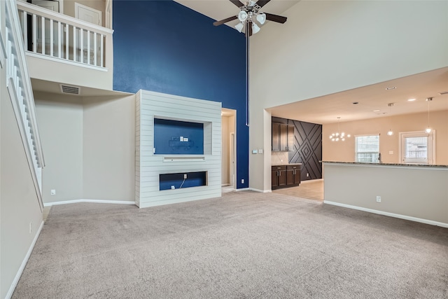 unfurnished living room with light colored carpet, a towering ceiling, a fireplace, and ceiling fan with notable chandelier