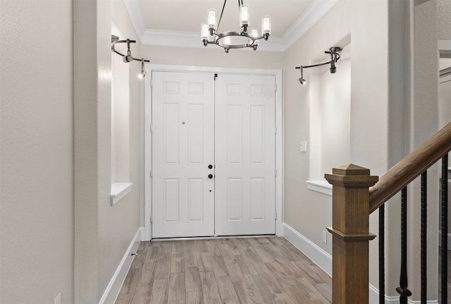 foyer entrance with ornamental molding, light hardwood / wood-style floors, and a notable chandelier