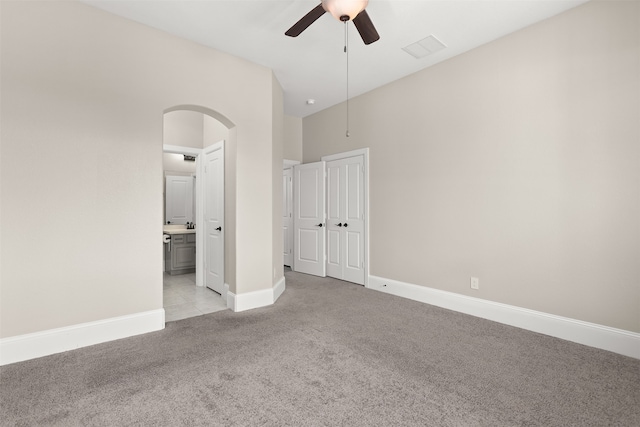 unfurnished bedroom featuring light colored carpet, ceiling fan, ensuite bath, and a closet