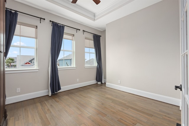 spare room with light wood-type flooring, ceiling fan, ornamental molding, and a raised ceiling