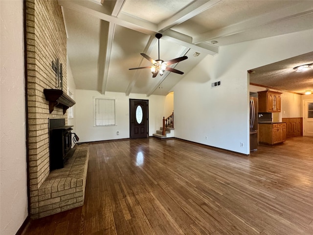 unfurnished living room with lofted ceiling with beams, a wood stove, a textured ceiling, hardwood / wood-style floors, and ceiling fan