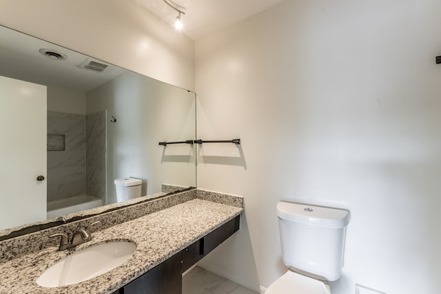 bathroom with a tile shower, toilet, and vanity