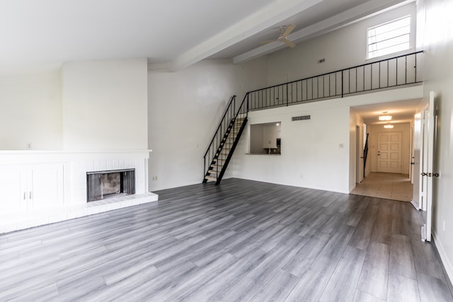 unfurnished living room with light hardwood / wood-style floors, a fireplace, beam ceiling, and a high ceiling