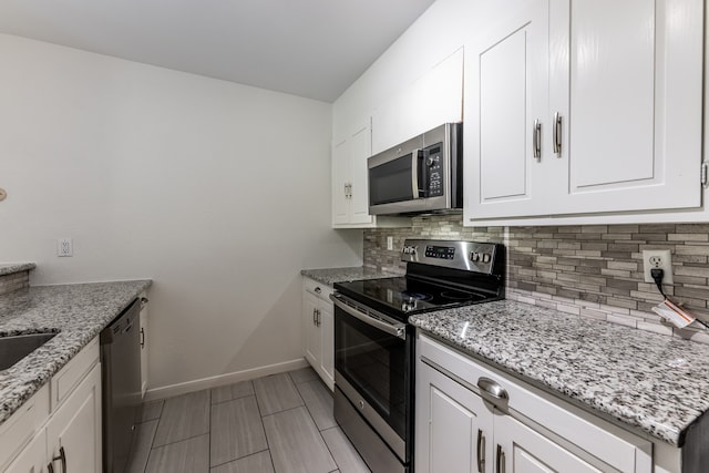 kitchen with appliances with stainless steel finishes, white cabinetry, light stone counters, and backsplash