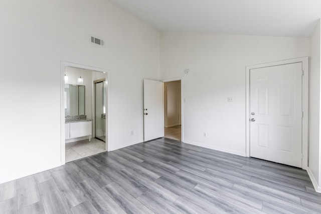 unfurnished bedroom featuring light hardwood / wood-style floors, ensuite bathroom, and high vaulted ceiling