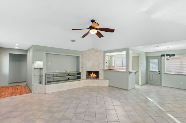 unfurnished living room with a tile fireplace, light tile patterned flooring, and ceiling fan with notable chandelier