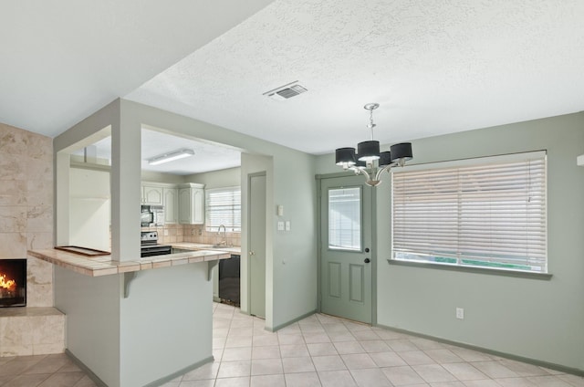 kitchen with tile countertops, a chandelier, a kitchen bar, a fireplace, and stainless steel range with electric cooktop