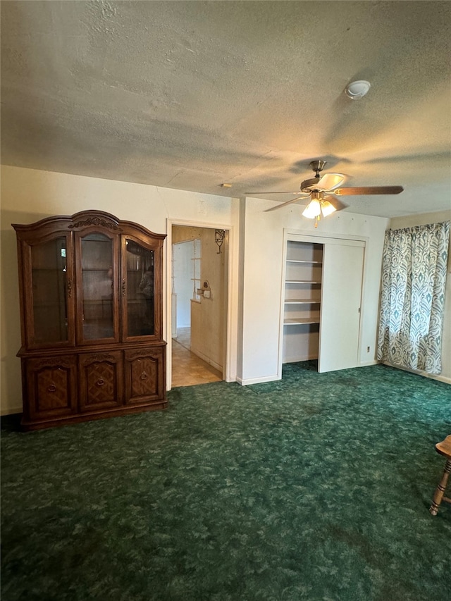 interior space with a textured ceiling, dark colored carpet, and ceiling fan