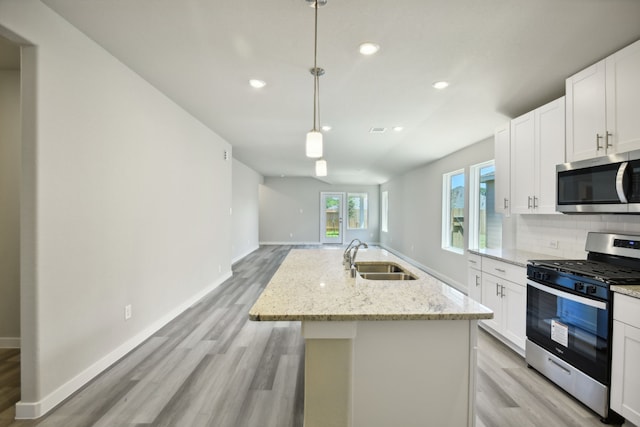 kitchen featuring an island with sink, appliances with stainless steel finishes, decorative light fixtures, and sink