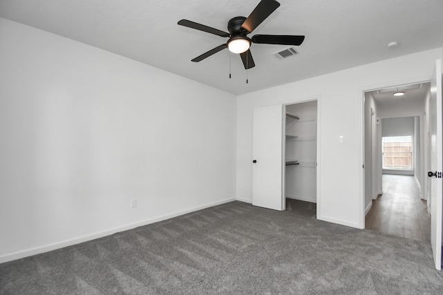 unfurnished bedroom featuring a closet, a walk in closet, dark colored carpet, and ceiling fan