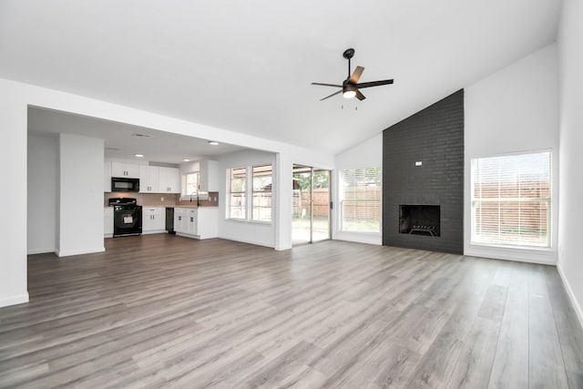 unfurnished living room featuring a fireplace, high vaulted ceiling, sink, ceiling fan, and light hardwood / wood-style flooring