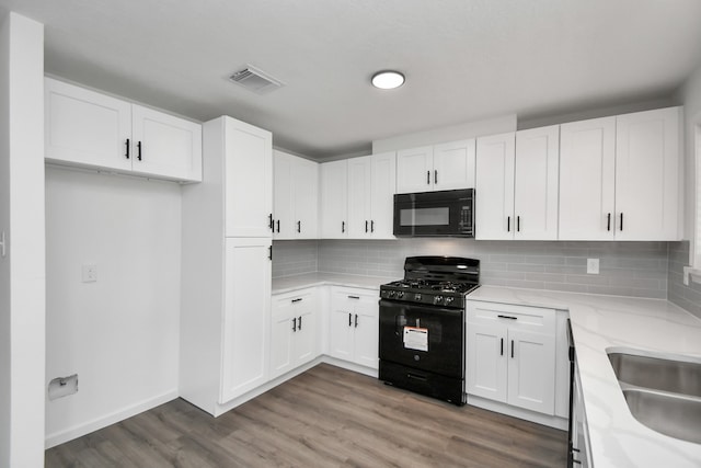 kitchen with black appliances, tasteful backsplash, light stone counters, white cabinetry, and hardwood / wood-style flooring