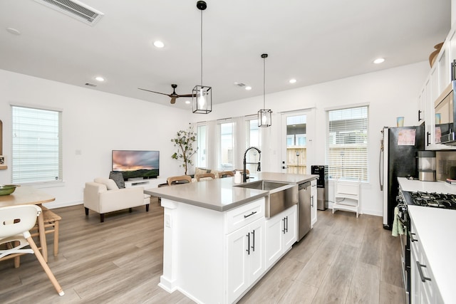 kitchen with stainless steel appliances, a center island with sink, decorative light fixtures, a wealth of natural light, and white cabinets