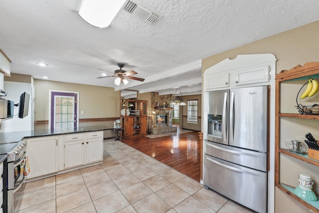 kitchen with appliances with stainless steel finishes, light hardwood / wood-style flooring, white cabinetry, and a stone fireplace