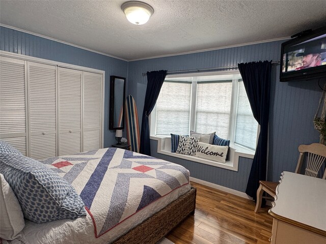 bedroom featuring a textured ceiling, a closet, ornamental molding, and wood-type flooring