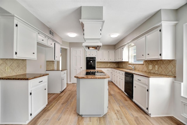 kitchen with dark stone countertops, black appliances, light hardwood / wood-style flooring, and a kitchen island