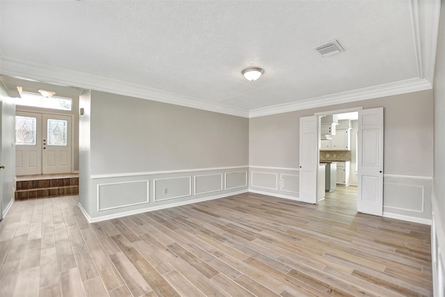 empty room with french doors, ornamental molding, a textured ceiling, and light wood-type flooring