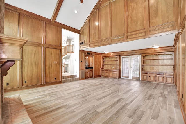 unfurnished living room with french doors, beamed ceiling, wooden walls, high vaulted ceiling, and light hardwood / wood-style flooring