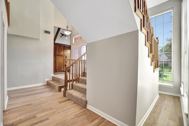 stairway with a towering ceiling, wood-type flooring, and ceiling fan