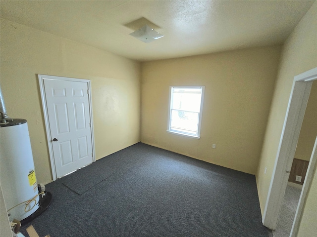 spare room featuring water heater and dark colored carpet