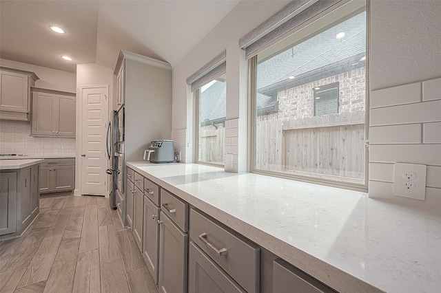 kitchen featuring light wood-type flooring, lofted ceiling, gray cabinets, decorative backsplash, and stainless steel refrigerator