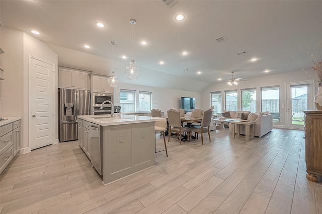 kitchen featuring a kitchen island with sink, a kitchen bar, light hardwood / wood-style flooring, stainless steel appliances, and decorative light fixtures