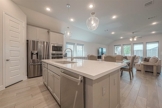 kitchen with sink, appliances with stainless steel finishes, vaulted ceiling, and a kitchen island with sink