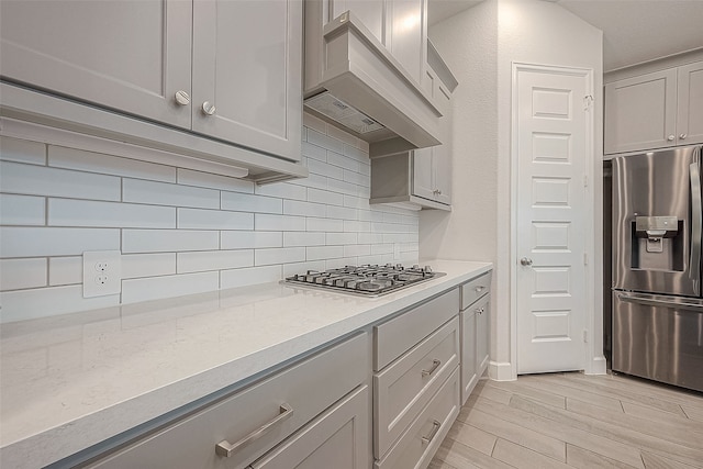 kitchen featuring gray cabinetry, appliances with stainless steel finishes, decorative backsplash, light hardwood / wood-style flooring, and premium range hood