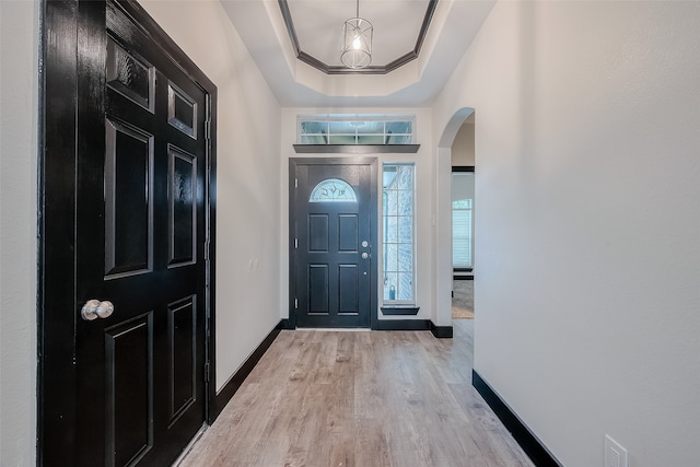 entrance foyer with a tray ceiling, crown molding, and light hardwood / wood-style flooring