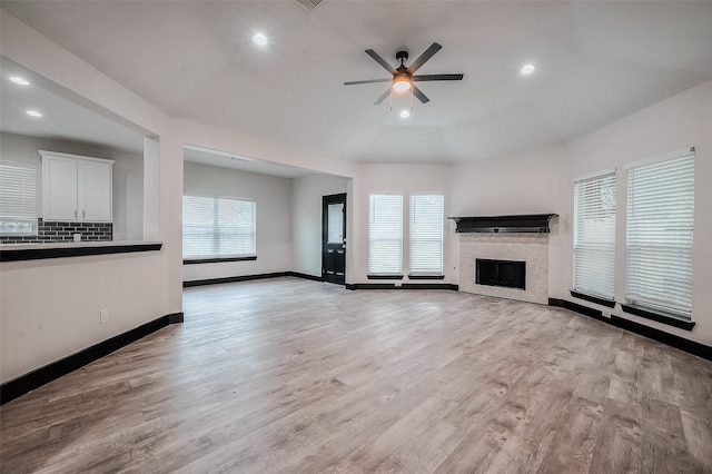 unfurnished living room with light wood-type flooring, a tiled fireplace, and ceiling fan