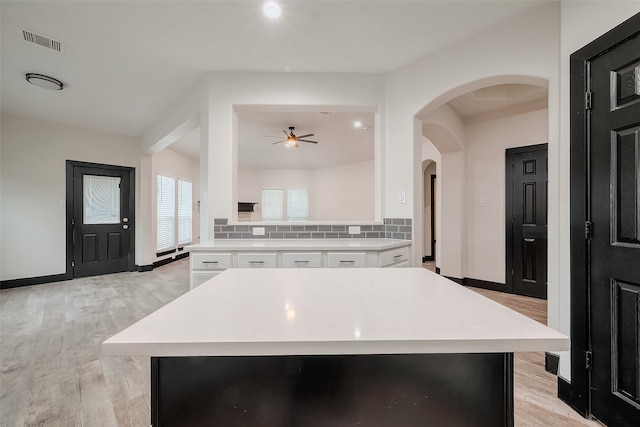 kitchen featuring white cabinets, light hardwood / wood-style floors, tasteful backsplash, and a center island