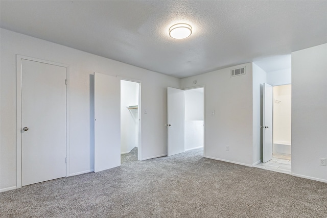 unfurnished bedroom with a closet, light carpet, a walk in closet, ensuite bathroom, and a textured ceiling