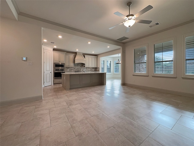 kitchen with stainless steel microwave, tasteful backsplash, a kitchen island with sink, custom range hood, and ceiling fan