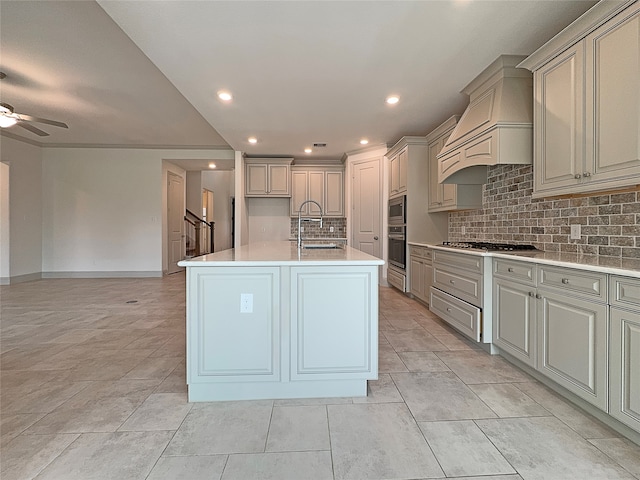 kitchen with a center island with sink, stainless steel appliances, backsplash, sink, and custom exhaust hood