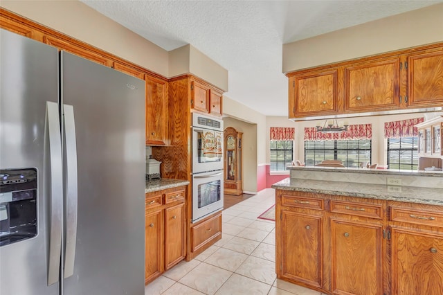 kitchen featuring light stone counters, stainless steel refrigerator with ice dispenser, a textured ceiling, light tile patterned floors, and double oven