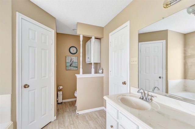 bathroom featuring a bath, vanity, a textured ceiling, hardwood / wood-style flooring, and toilet